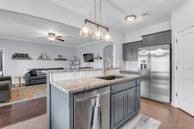 kitchen with appliances with stainless steel finishes, gray cabinetry, ceiling fan, a kitchen island with sink, and sink