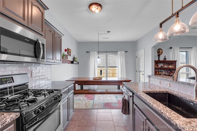 kitchen with sink, decorative backsplash, light stone countertops, appliances with stainless steel finishes, and dark brown cabinets