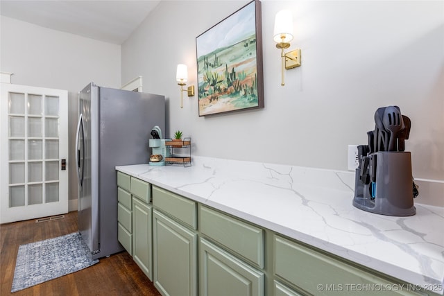 kitchen with dark hardwood / wood-style floors, light stone counters, green cabinetry, and stainless steel refrigerator