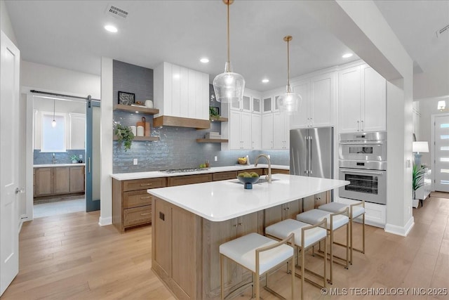 kitchen with white cabinetry, stainless steel appliances, a barn door, and a center island with sink