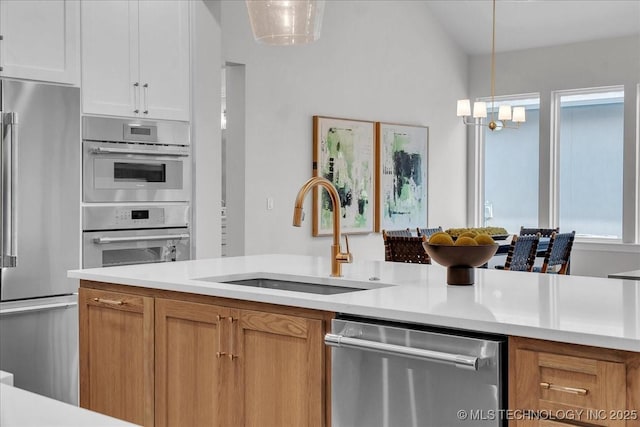 kitchen with sink, hanging light fixtures, a notable chandelier, stainless steel appliances, and white cabinets