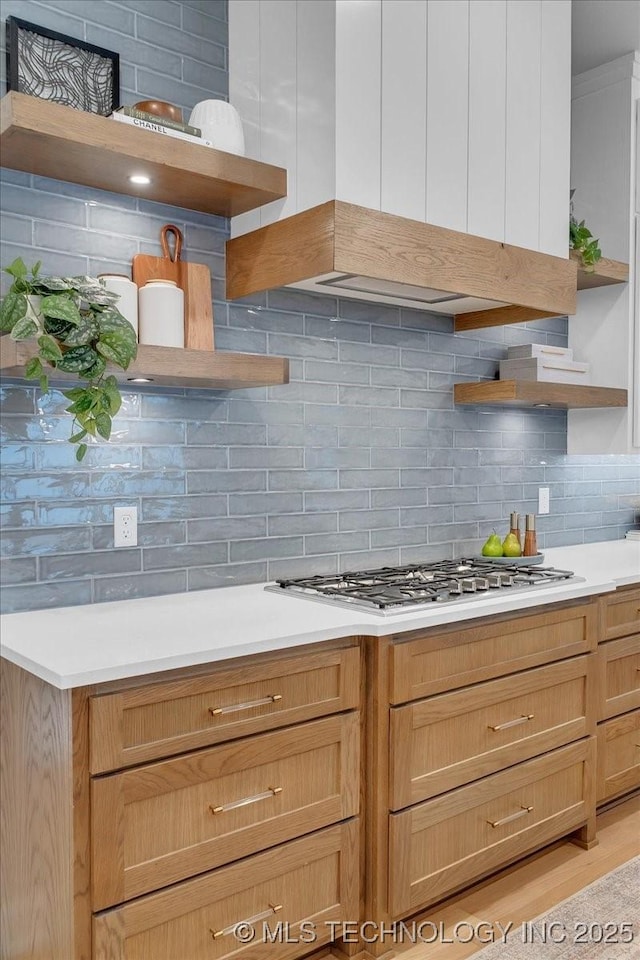 kitchen with stainless steel gas stovetop, custom range hood, backsplash, and light wood-type flooring