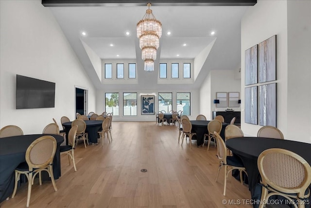 living room with beamed ceiling, a chandelier, light wood-type flooring, and a high ceiling