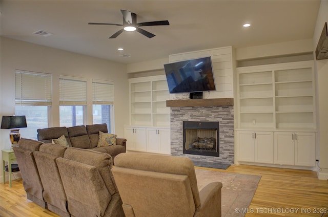 living room featuring a fireplace, light wood-type flooring, built in features, and ceiling fan