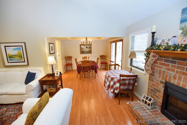 living room featuring a notable chandelier, wood-type flooring, lofted ceiling, and a brick fireplace