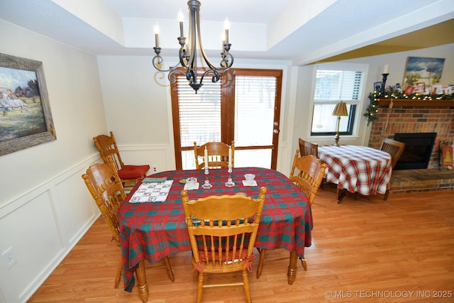 dining area featuring an inviting chandelier, light hardwood / wood-style flooring, a brick fireplace, and a tray ceiling