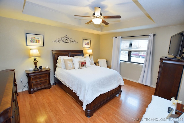 bedroom with a tray ceiling, ceiling fan, and light hardwood / wood-style floors