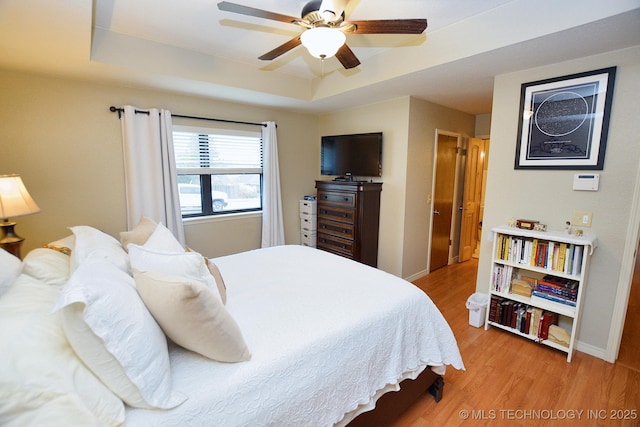 bedroom with a raised ceiling, ceiling fan, and light hardwood / wood-style flooring