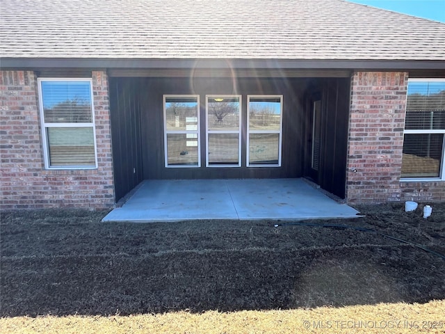 doorway to property featuring a patio area, a shingled roof, and brick siding