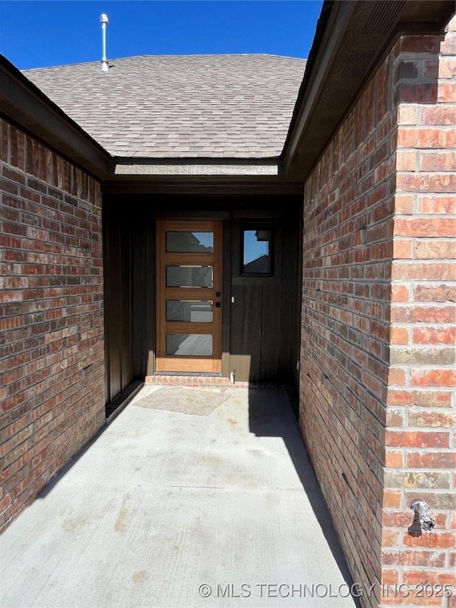 view of exterior entry featuring a shingled roof and brick siding