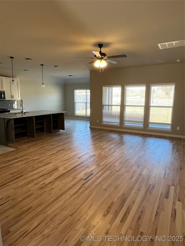 unfurnished living room with baseboards, a sink, light wood-style flooring, and a ceiling fan