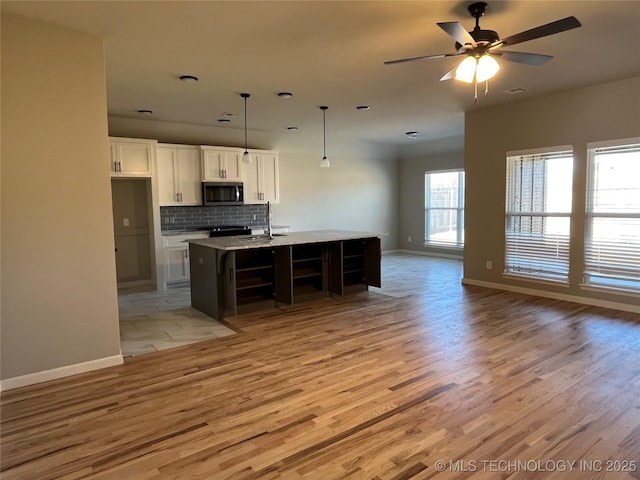 kitchen featuring tasteful backsplash, stainless steel microwave, open floor plan, white cabinetry, and light wood-type flooring