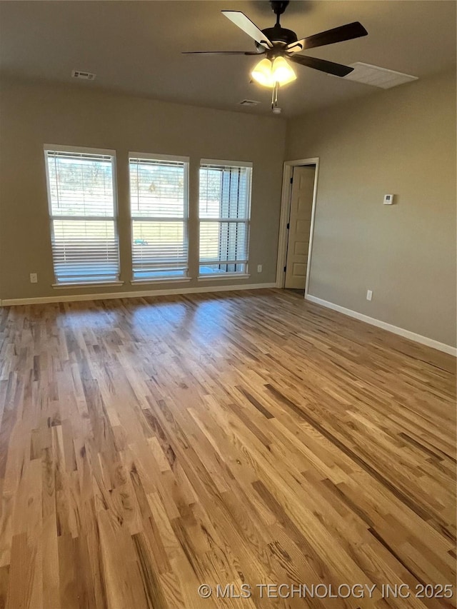 unfurnished room with a ceiling fan, wood finished floors, visible vents, and baseboards