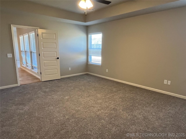 spare room with visible vents, a ceiling fan, baseboards, dark colored carpet, and a tray ceiling