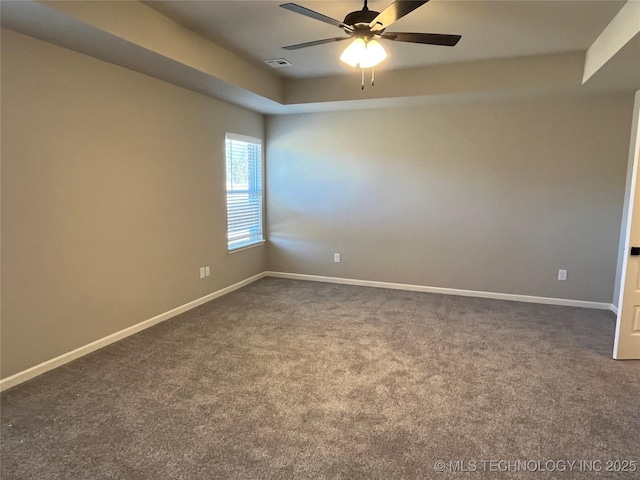 spare room featuring baseboards, a raised ceiling, and dark colored carpet