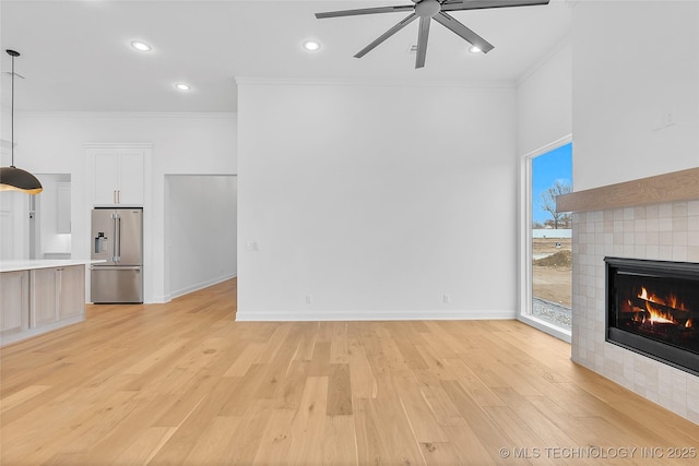 unfurnished living room featuring ceiling fan, a tiled fireplace, light wood-type flooring, and crown molding