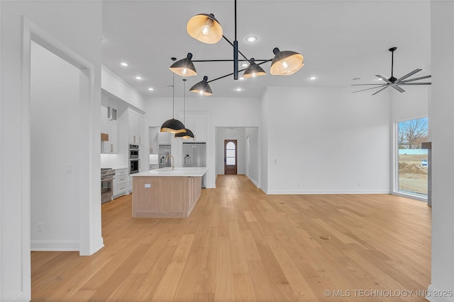 kitchen featuring ceiling fan, a kitchen island with sink, white cabinets, hanging light fixtures, and light hardwood / wood-style flooring