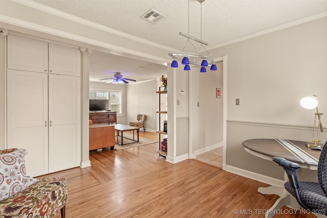 interior space with ceiling fan, crown molding, light wood-type flooring, and a textured ceiling