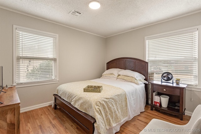 bedroom with multiple windows, light hardwood / wood-style floors, and a textured ceiling