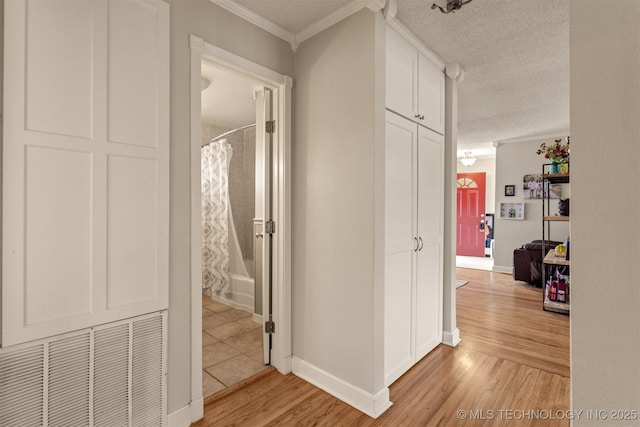 hall with a textured ceiling, light hardwood / wood-style floors, and ornamental molding