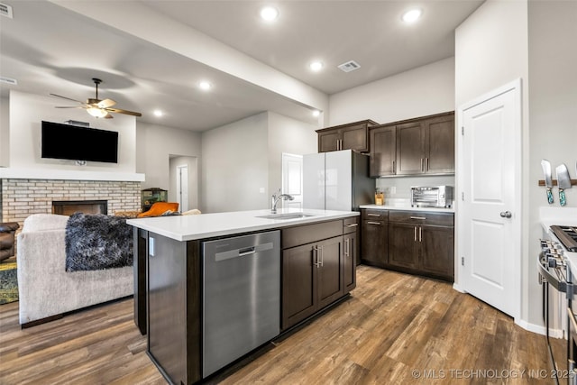 kitchen with a center island with sink, sink, a fireplace, appliances with stainless steel finishes, and dark brown cabinetry