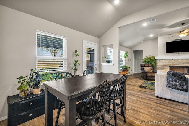 dining space featuring a fireplace, wood-type flooring, ceiling fan, and lofted ceiling