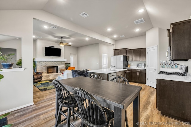 dining room with light wood-type flooring, a brick fireplace, ceiling fan, sink, and lofted ceiling