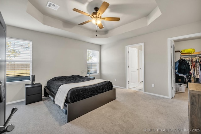 carpeted bedroom with a raised ceiling, a spacious closet, a closet, and ceiling fan