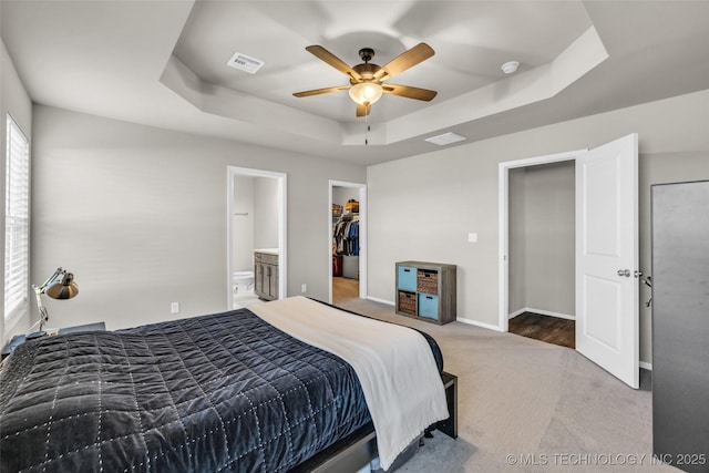 bedroom with carpet, a walk in closet, ensuite bath, ceiling fan, and a tray ceiling