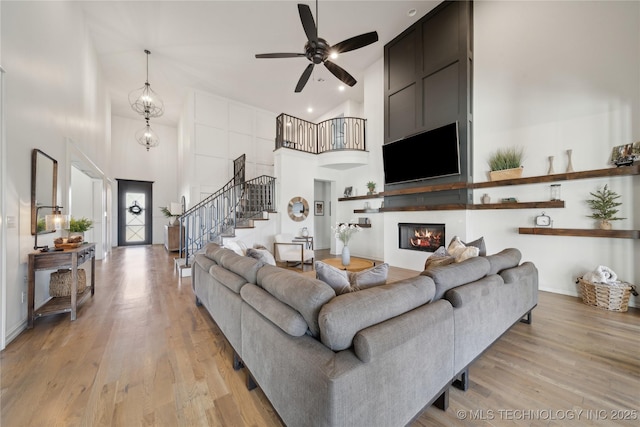 living room featuring ceiling fan, a large fireplace, a high ceiling, and light hardwood / wood-style flooring