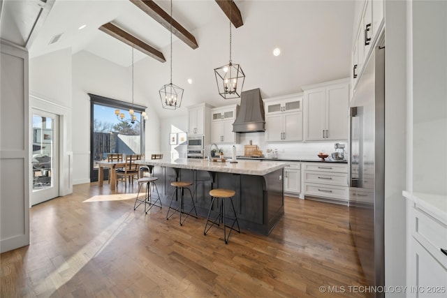 kitchen with a center island with sink, a kitchen bar, white cabinetry, hanging light fixtures, and custom range hood