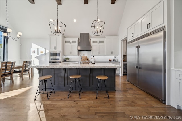 kitchen featuring white cabinets, custom range hood, built in appliances, and a kitchen island with sink