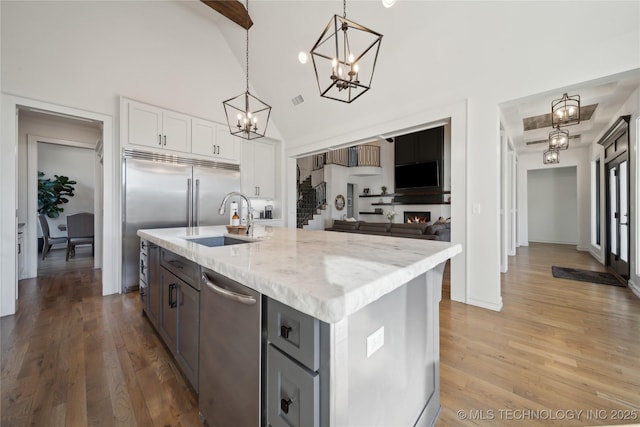 kitchen with a center island with sink, pendant lighting, a large fireplace, sink, and white cabinetry