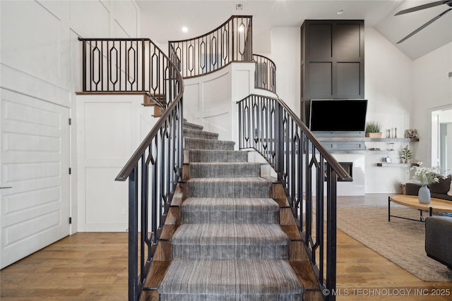 stairs with ceiling fan, hardwood / wood-style flooring, and high vaulted ceiling