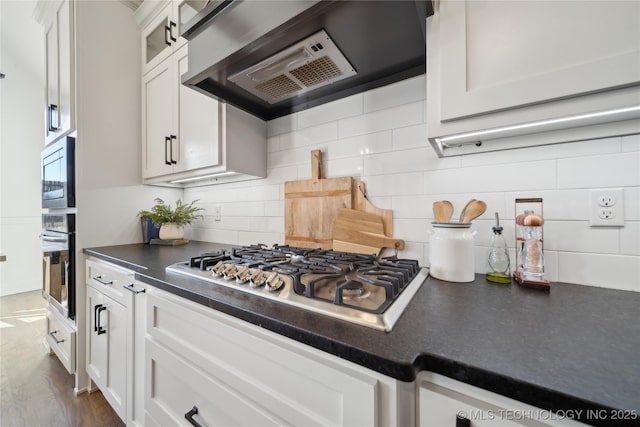 kitchen with decorative backsplash, wall chimney range hood, stainless steel appliances, and white cabinetry