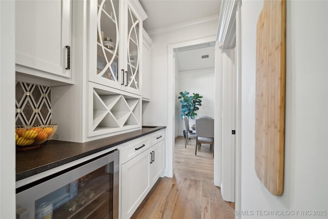 bar featuring white cabinets, beverage cooler, backsplash, light wood-type flooring, and crown molding