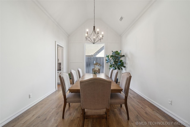 dining room with an inviting chandelier, ornamental molding, hardwood / wood-style floors, and high vaulted ceiling