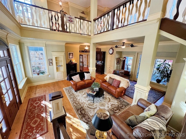 living room with ceiling fan, light hardwood / wood-style floors, a high ceiling, and decorative columns