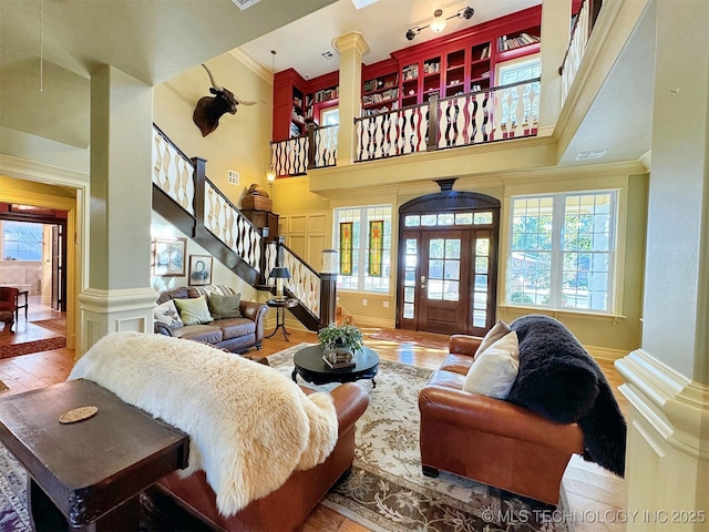 living room with a healthy amount of sunlight, a towering ceiling, crown molding, and decorative columns