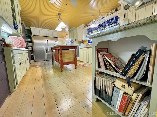 kitchen with pendant lighting, light hardwood / wood-style flooring, a kitchen island, a breakfast bar area, and stainless steel refrigerator