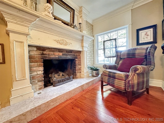 living area with hardwood / wood-style floors, ornamental molding, and a brick fireplace