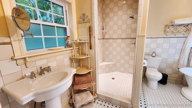 bathroom featuring sink, toilet, tiled shower, and tile walls