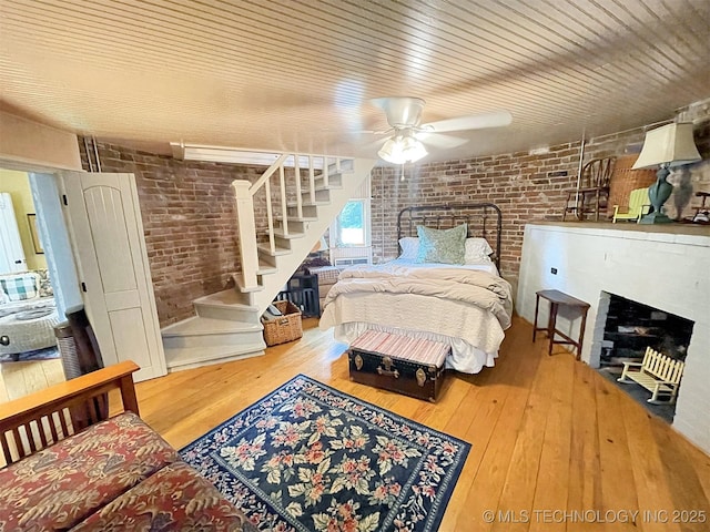 bedroom with ceiling fan, wood-type flooring, and brick wall