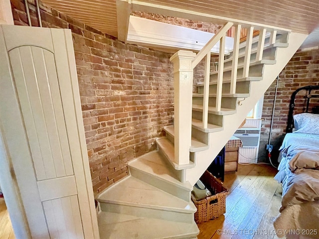 stairway featuring hardwood / wood-style floors and brick wall