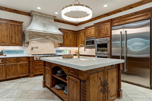 kitchen featuring sink, tasteful backsplash, built in appliances, an island with sink, and custom range hood