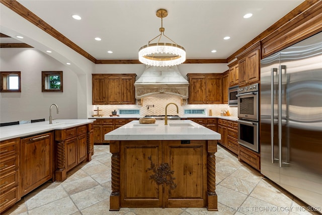 kitchen featuring hanging light fixtures, a kitchen island with sink, built in appliances, decorative backsplash, and custom range hood