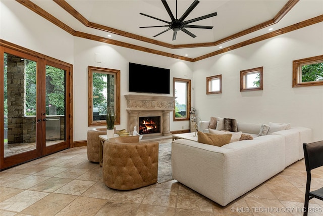 living room featuring french doors, a towering ceiling, a tray ceiling, ceiling fan, and crown molding