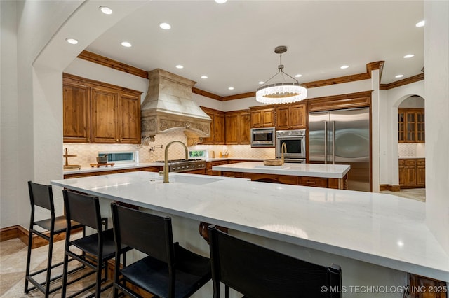 kitchen featuring custom exhaust hood, backsplash, sink, built in appliances, and a kitchen bar