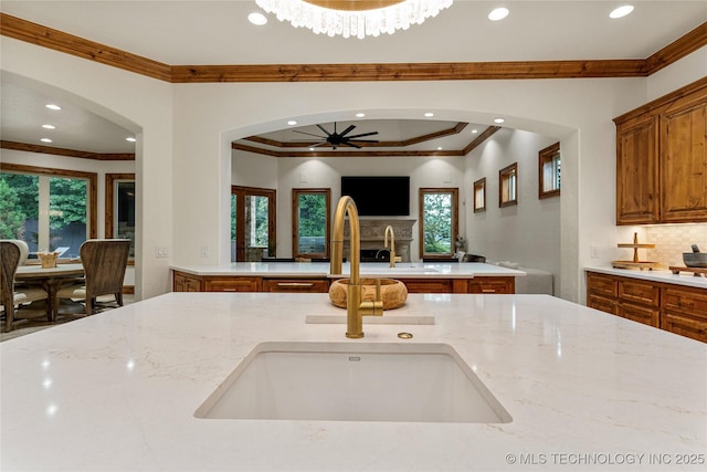 kitchen featuring light stone countertops, ceiling fan, crown molding, and sink