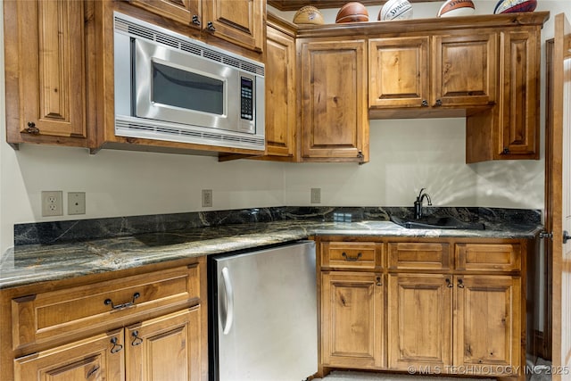 kitchen with stainless steel microwave, dark stone counters, fridge, and sink